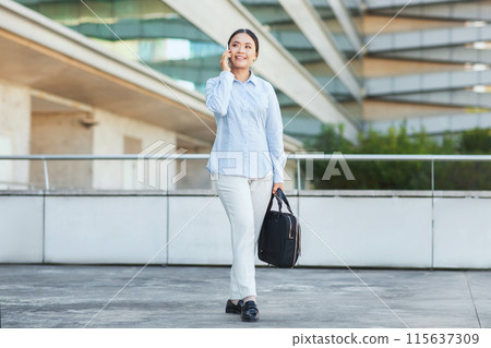 An Asian businesswoman is seen talking on the phone in a professional setting. She appears focused and engaged in the conversation, showcasing her multitasking skills. An Asian businesswoman is seen talking on the phone in a professional setting. She appears focused and engaged in the conversation, showcasing her multitasking skills. 115637309