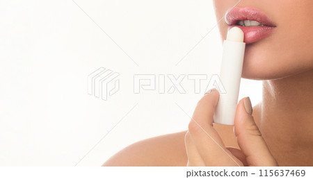 Cropped of woman is carefully applying lip balm to her lips. She is holding the lip balm stick in one hand and using her other hand to glide it smoothly over her lips, copy space 115637469