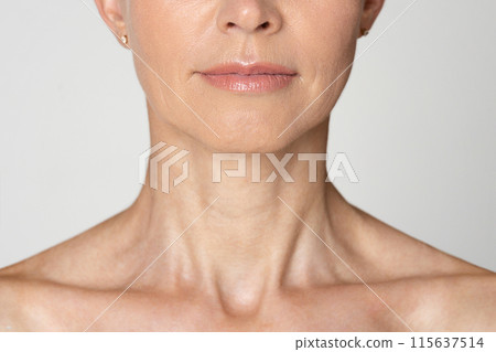 Cropped of a womans neck and chin. The woman is wearing a light color shirt and has a neutral expression. Her skin is smooth and wrinkle-free. Cropped of a womans neck and chin. The woman is wearing a light color shirt and has a neutral expression. Her skin is smooth and wrinkle-free. 115637514