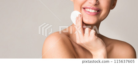 A smiling woman uses a cotton pad to clean her face in a well-lit room. She appears content and happy, focusing on her skincare routine, cropped. copy space A smiling woman uses a cotton pad to clean her face in a well-lit room. She appears content and happy, focusing on her skincare routine, cropped. copy space 115637605