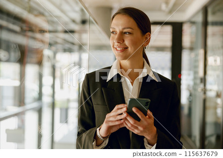 Smiling businesswoman in modern office confidently using a smartphone to communicate and work Smiling businesswoman in modern office confidently using a smartphone to communicate and work 115637679