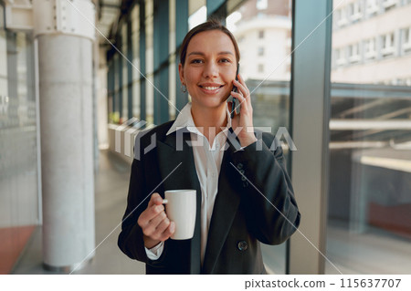 A modern office setting with a young professional woman holding coffee and talking on the phone A modern office setting with a young professional woman holding coffee and talking on the phone 115637707