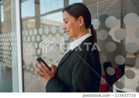 A businesswoman in a modern office uses a smartphone to stay connected and productive A businesswoman in a modern office uses a smartphone to stay connected and productive 115637710