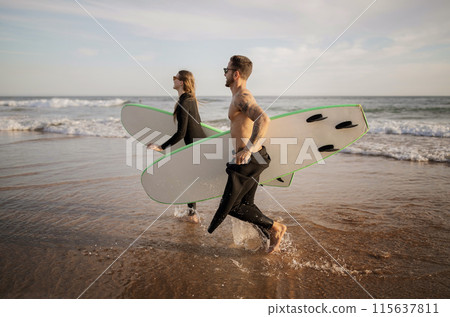 Happy Young Friends Surfing Together On The Beach, Cheerful Millennial Man And Woman Running With Surfboards Near Ocean, Sporty Couple Wearing Wetsuits Having Fun, Enjoying Water Sports, Copy Space Happy Young Friends Surfing Together On The Beach, Cheerful Millennial Man And Woman Running With Surfboards Near Ocean, Sporty Couple Wearing Wetsuits Having Fun, Enjoying Water Sports, Copy Space 115637811