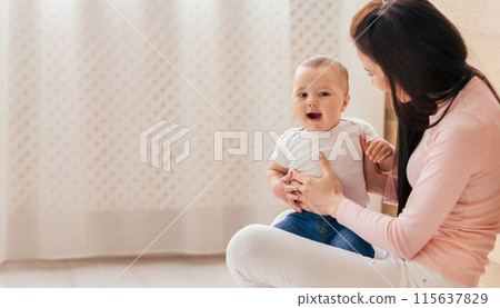 A woman sitting down and cradling a baby in her lap. The baby appears content and secure in her arms, while the woman gazes down at the child with a soft expression. A woman sitting down and cradling a baby in her lap. The baby appears content and secure in her arms, while the woman gazes down at the child with a soft expression. 115637829