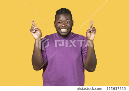 Making cherished wish. Young cheerful black man posing with crossed fingers for luck standing on yellow studio background, smiling to camera. Happy guy makes finger crossing gesture Making cherished wish. Young cheerful black man posing with crossed fingers for luck standing on yellow studio background, smiling to camera. Happy guy makes finger crossing gesture 115637833