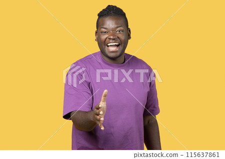Greeting concept. Smiling African American Man holding out his hand for handshake on yellow studio background. Positive guy in purple t-shirt making agreement or deal, offering partnership 115637861