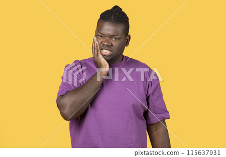 Toothache Issue. Unhappy black man suffering from tooth ache, having gum problems, touching his cheek on yellow background. African American guy having sensitive teeth, suffering from dental pain 115637931