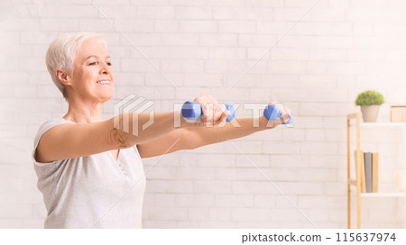 An older woman is actively exercising in a white room, lifting dumbbells to strengthen her muscles and improve her physical fitness 115637974