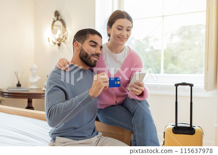 Ecommerce. Cheerful Couple With Credit Card And Smartphone Booking Travel Accomodation Online, Shopping And Making Payment Via Mobile Bank App Sitting In Modern Hotel Bedroom 115637978