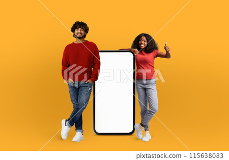 A man and a woman are standing next to a blank screen, both posing as if they are presenting something. The blank screen offers a versatile space for text or images. 115638083