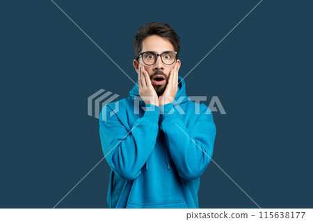 A man wearing a blue hoodie is covering his face with his hands in this candid street photograph. The mans expression is obscured, adding a sense of mystery to the scene. A man wearing a blue hoodie is covering his face with his hands in this candid street photograph. The mans expression is obscured, adding a sense of mystery to the scene. 115638177