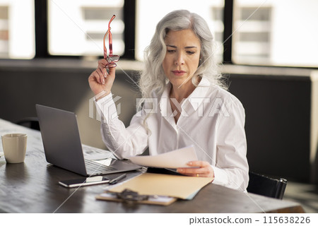 Businesswoman Doing Paperwork Writing Reports, Looking At Papers And Documents Holding Glasses, Sitting At Table With Laptop In Modern Office. Manager Lady Reading Proposals And Resume At Workplace 115638226