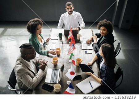 International Business Conference. Team Of Five Diverse Businessmen And Businesswomen Having Corporate Meeting, Sitting With Their Computers At Table With Different Countries Flags In Modern Office International Business Conference. Team Of Five Diverse Businessmen And Businesswomen Having Corporate Meeting, Sitting With Their Computers At Table With Different Countries Flags In Modern Office 115638239