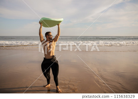 Full Length Shot Of Professional Male Surfer In Wetsuit Holding Surfboard Above Head While Standing On The Beach In Summer, Handsome Athletic Guy Surfing On Sunset, Enjoying Water Sports, Copy Space Full Length Shot Of Professional Male Surfer In Wetsuit Holding Surfboard Above Head While Standing On The Beach In Summer, Handsome Athletic Guy Surfing On Sunset, Enjoying Water Sports, Copy Space 115638329