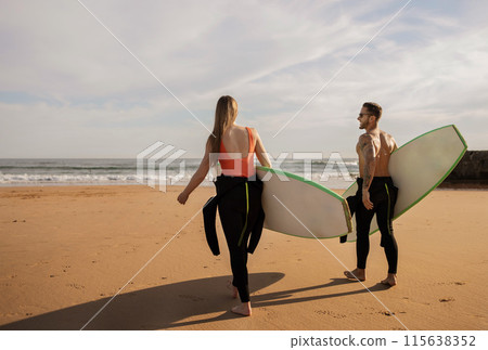 Watersports Concept. Young Couple With Surfboards Going Into The Ocean, Smiling Surfers Friends Wearing Wetsuits Walking On The Beach, Enjoying Surfing Together, Waiting For High Waves, Copy Space Watersports Concept. Young Couple With Surfboards Going Into The Ocean, Smiling Surfers Friends Wearing Wetsuits Walking On The Beach, Enjoying Surfing Together, Waiting For High Waves, Copy Space 115638352