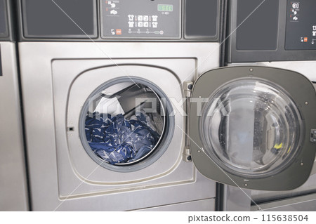 Public Laundry. Shot Of Modern Industrial Washing Machine With Opened Door And Loaded Clothes At Laundrette Indoors. Public Convenience Service, Automatic Laundromat Room Concept 115638504