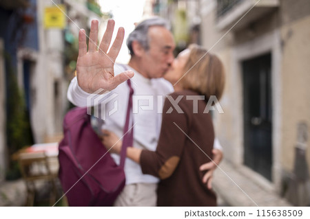 Don't Disturb. Loving Senior Couple Kissing Gesturing Stop To Camera, Enjoying Love And Vacation, Posing Standing With Backpack In Lisbon Outdoor. Golden Travel And Romance Concept. Selective Focus 115638509
