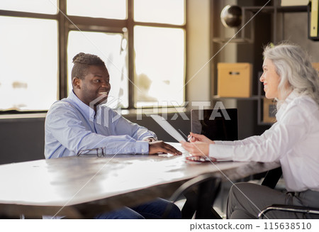 Job Interview, Business Meeting. HR Manager Lady Talking With Happy Black Man About Employment Sitting At Desk In Office Interior. Corporate Career Growth Concept. Selective Focus 115638510