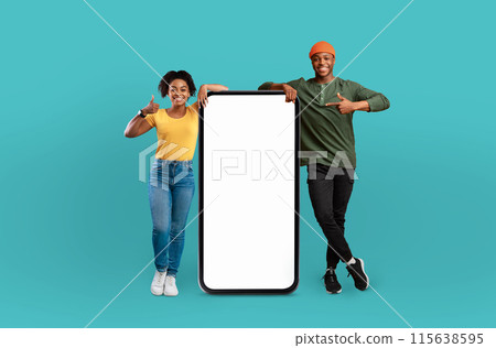 A young Black man and woman are standing together, holding up a blank phone screen. They are looking at the screen with focused expressions, possibly sharing information or taking a photo. A young Black man and woman are standing together, holding up a blank phone screen. They are looking at the screen with focused expressions, possibly sharing information or taking a photo. 115638595