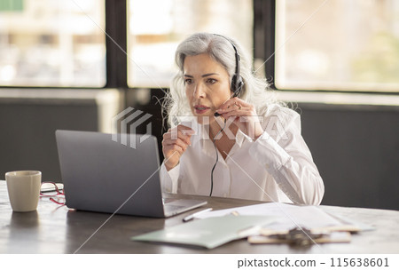 Hotline Operator Woman Wearing Headset Making Video Call, Providing Assistance And Support To Customers Sitting At Laptop Solving Problems In Office. Corporate Communication, Business Calls Hotline Operator Woman Wearing Headset Making Video Call, Providing Assistance And Support To Customers Sitting At Laptop Solving Problems In Office. Corporate Communication, Business Calls 115638601
