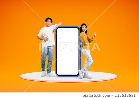 Cheerful chinese millennials casual man and woman posing on platform by big phone with white empty screen, showing thumb up, isolated on orange background, blank space. Great online offer Cheerful chinese millennials casual man and woman posing on platform by big phone with white empty screen, showing thumb up, isolated on orange background, blank space. Great online offer 115638651