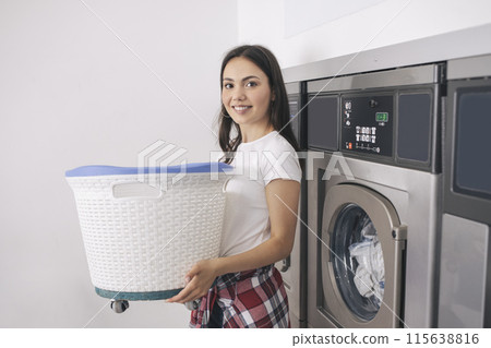 Laundromat Room. Happy Young Lady In Casual Doing Laundry At Public Laundrette Indoors, Posing Holding Basket With Dirty Clothes Near Industrial Washing Machines And Smiling To Camera Laundromat Room. Happy Young Lady In Casual Doing Laundry At Public Laundrette Indoors, Posing Holding Basket With Dirty Clothes Near Industrial Washing Machines And Smiling To Camera 115638816