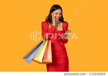 A woman in a vibrant red dress is preoccupied with her smartphone while holding multiple shopping bags in her hands. She seems engrossed in her device, potentially checking messages or making plans. 115638826