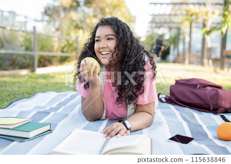 Cheerful Latin Student Woman Learning And Eating Apple Fruit Enjoying Picnic At Park Outdoor. Young Lady Having Healthy Snack While Reading Books And Doing College Homework Lying On Blanket Outside Cheerful Latin Student Woman Learning And Eating Apple Fruit Enjoying Picnic At Park Outdoor. Young Lady Having Healthy Snack While Reading Books And Doing College Homework Lying On Blanket Outside 115638846