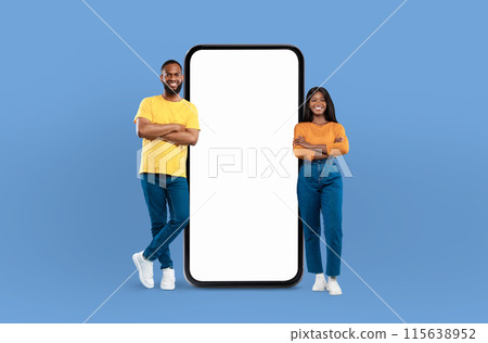 Black couple positioned next to a blank screen while standing against a blue background. They appear to be engaged in a presentation or discussion, with the screen ready for content to be displayed. 115638952