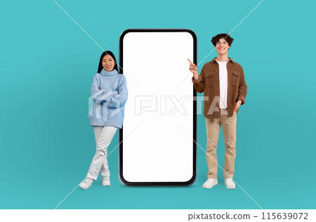Illuminated by the cool blue backdrop, the multiracial young man and woman share a smile, enhancing the visual appeal of the blank smartphone screen beside them. Illuminated by the cool blue backdrop, the multiracial young man and woman share a smile, enhancing the visual appeal of the blank smartphone screen beside them. 115639072