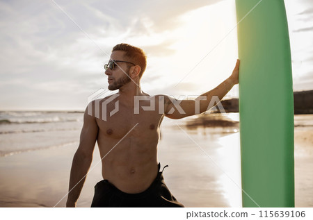Portrait of handsome young man holding surfboard at the beach, professional surfer guy in stylish eyeglasses posing on sunset, shirtless millennial male standing on ocean shore, ready for surfing Portrait of handsome young man holding surfboard at the beach, professional surfer guy in stylish eyeglasses posing on sunset, shirtless millennial male standing on ocean shore, ready for surfing 115639106