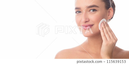 A woman is applying a facial cleanser to her face, rubbing it in gentle circular motions to remove dirt and impurities. The cleanser foams up as she massages it into her skin, panorama, copy space 115639153