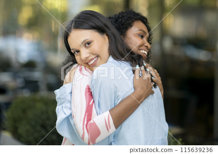 Cheerful Multiethnic Female Friends Embracing After Meeting On City Street, Two Beautiful Young Women Happy To See Each Other, Multicultural Besties Hugging And Smiling, Enjoying Outdoor Meet 115639236