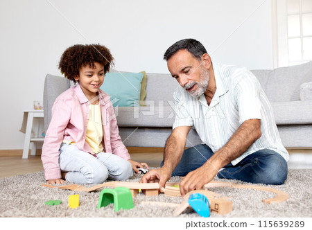 Multigenerational Playtime. Smiling Hispanic Grandfather and Little Grandson Enjoying Toy Fun, Playing And Bonding In Modern Living Room Interior, Sitting On Floor at Home Multigenerational Playtime. Smiling Hispanic Grandfather and Little Grandson Enjoying Toy Fun, Playing And Bonding In Modern Living Room Interior, Sitting On Floor at Home 115639289