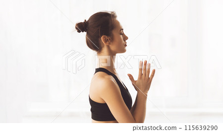 A woman is standing in a yoga pose with her hands together, focusing on balance and strength. She is practicing mindfulness and flexibility while holding the pose steadily. A woman is standing in a yoga pose with her hands together, focusing on balance and strength. She is practicing mindfulness and flexibility while holding the pose steadily. 115639290