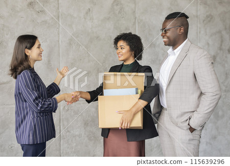 Employment. New Employee Lady Holding Carton Box Handshaking With Colleague And HR Manager Over Gray Office Wall Indoor. Coworkers Welcoming New Staff Member At Workplace. Hiring And Headhunting Employment. New Employee Lady Holding Carton Box Handshaking With Colleague And HR Manager Over Gray Office Wall Indoor. Coworkers Welcoming New Staff Member At Workplace. Hiring And Headhunting 115639296