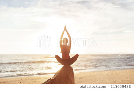 Calm young caucasian lady enjoy morning workout, breathing exercises, meditation, practicing yoga in lotus position on stone on sea beach. Lifestyle and body care, balance outdoor 115639488