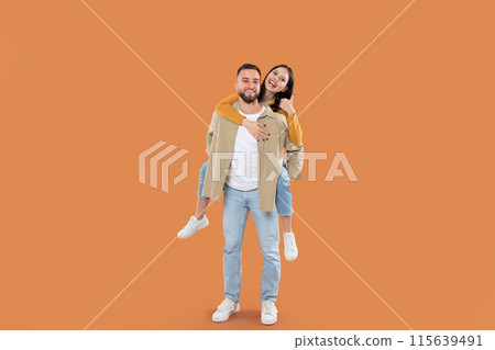 A man is carrying a woman on his back. The mans arms are wrapped around the woman thighs, holding her securely, appear to be in motion, possibly walking or engaging in a playful activity. A man is carrying a woman on his back. The mans arms are wrapped around the woman thighs, holding her securely, appear to be in motion, possibly walking or engaging in a playful activity. 115639491