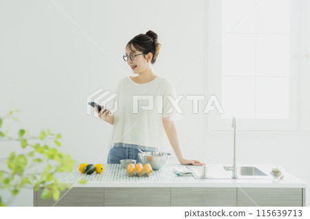 年輕女子在廚房看智慧型手機 年輕女子在廚房看智慧型手機 115639713