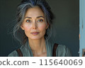 Beautiful asian woman with gray hair in crinkle shirt indoors during daytime against blank grey wall 115640069