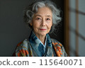 Elderly woman in blue and orange flowers kimono, grey wall and traditional japanese shoji screen 115640071