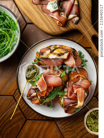 Appetizer toasts with prosciutto, pesto sauce, cheese and arugula on a table on a table 115640517