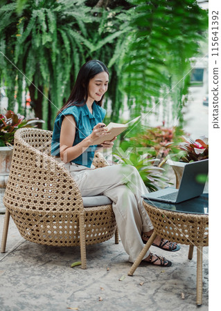 A woman is sitting in a chair with a laptop open in front of her. She is smiling and she is enjoying her time. The scene suggests a relaxed and leisurely atmosphere A woman is sitting in a chair with a laptop open in front of her. She is smiling and she is enjoying her time. The scene suggests a relaxed and leisurely atmosphere 115641392