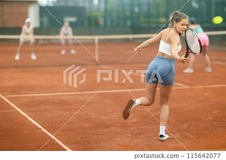 Emotional fit young girl playing doubles tennis on outdoor court 115642077
