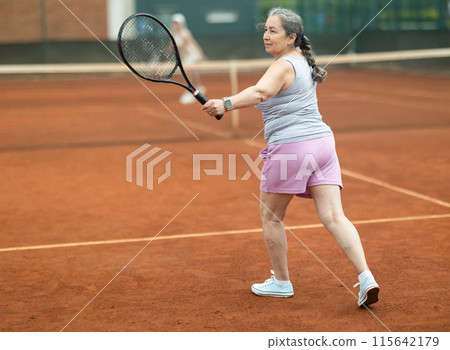 Elderly woman making serve while playing tennis 115642179