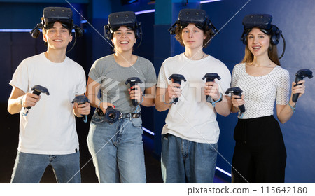 Cheerful youth with handheld controllers and VR glasses in virtual reality room 115642180