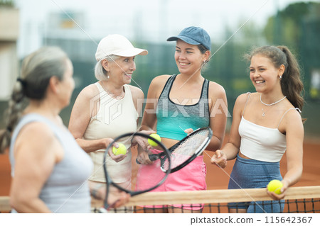 Laughing girls and elderly women with tennis rackets talking on court Laughing girls and elderly women with tennis rackets talking on court 115642367