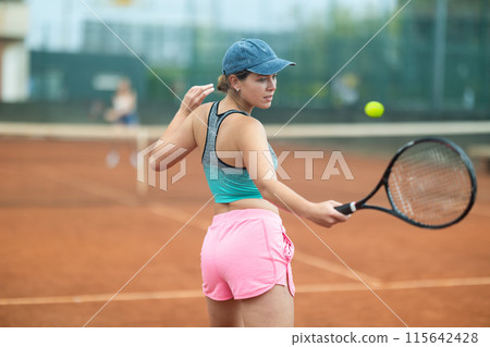 Young woman making serve while playing tennis 115642428