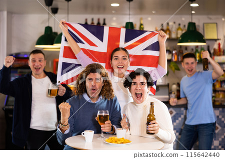 Company of joyful sports supporters waving flag of Great Britain and celebrating victory of favotite team in pub 115642440